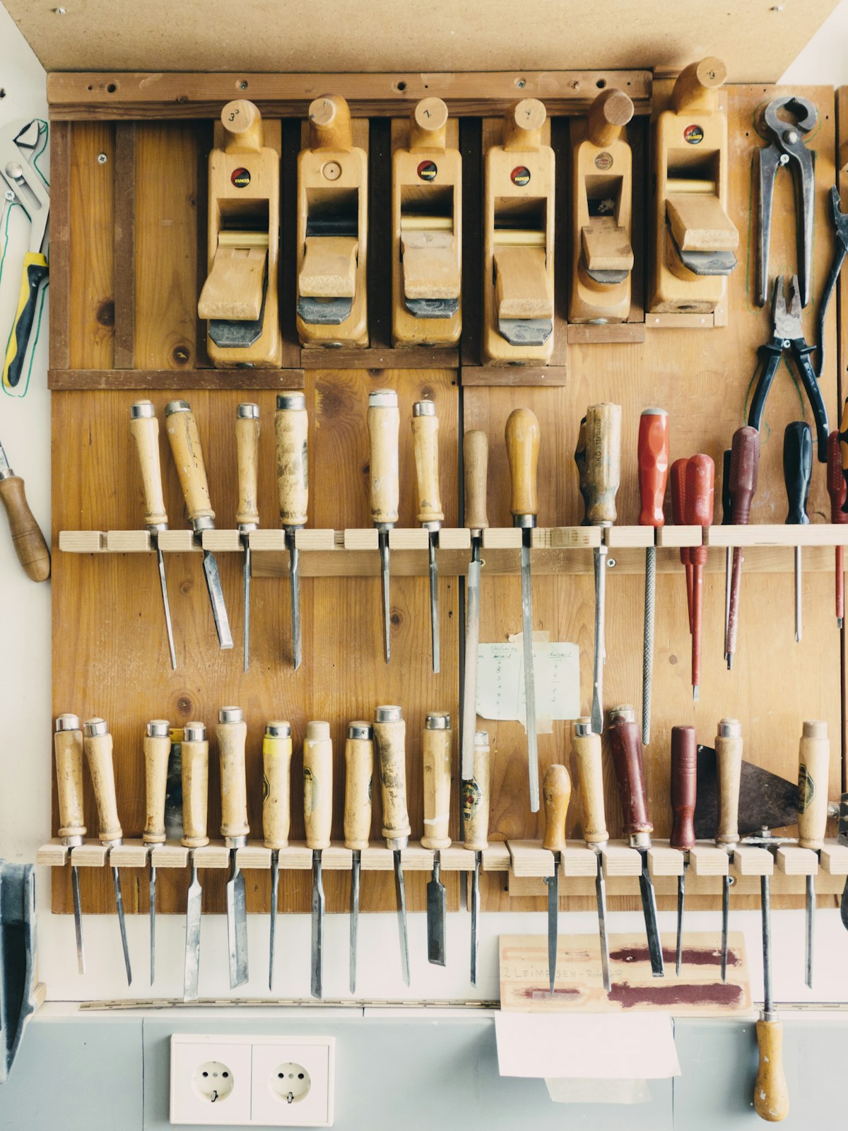 Hand tools arranged on a craftsman's workshop wall &mdash; chisels, hand planes, and pliers.